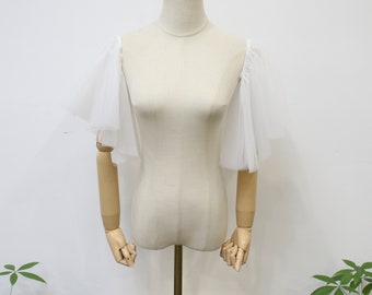 May include: White tulle fabric sleeves on a dress form. The sleeves are gathered at the shoulders and have a ruffled edge.