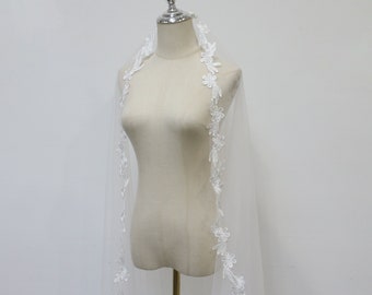 May include: White bridal veil with a delicate floral lace trim. The veil is draped over a mannequin.