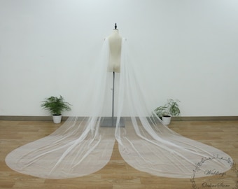 May include: A white tulle bridal cape with a long train. The cape is draped over a dress form and the train is spread out on the floor.