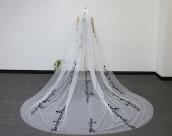 May include: A white tulle wedding veil with black floral embroidery. The veil is long and flowing, with a delicate design.