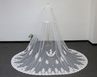 May include: A white bridal veil with a scalloped lace trim and pearl embellishments. The veil is long and flowing, with a delicate floral pattern.