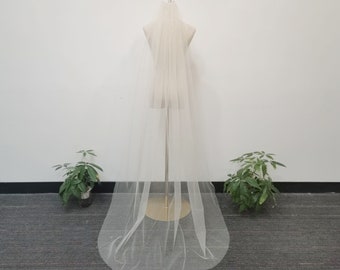 May include: A long, white tulle wedding veil with a delicate sparkle. The veil is displayed on a mannequin and is hanging down to the floor.