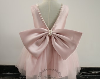 Puede incluir: Un vestido de tul y satén rosa con un gran lazo en la espalda. El vestido tiene una espalda en forma de V y está decorado con cuentas de perlas.