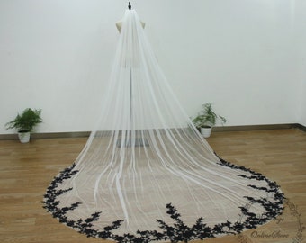 May include: A long white bridal veil with a black floral lace trim. The veil is draped over a mannequin and is shown from the back.