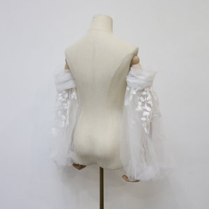 May include: White tulle bridal sleeves with delicate floral embroidery. The sleeves are gathered at the elbow and have a flowing, romantic look.