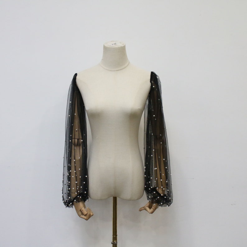 May include: Black sheer mesh sleeves with pearl embellishments. The sleeves are long and have a gathered cuff.