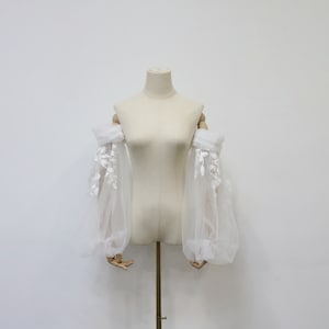 May include: White tulle off-the-shoulder sleeves with delicate floral lace embroidery. The sleeves are gathered at the wrist and have a puffed look.