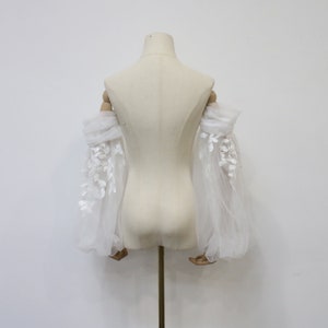 May include: White tulle bridal sleeves with delicate floral lace embroidery. The sleeves are gathered at the elbow and have a flowing, romantic look.