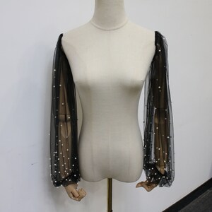 May include: Black sheer sleeves with pearl embellishments. The sleeves are made of a delicate mesh fabric and are adorned with small, white pearls.