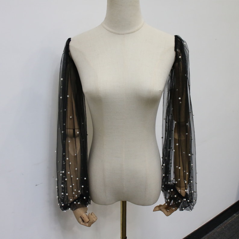 May include: Black sheer sleeves with pearl embellishments. The sleeves are made of a delicate mesh fabric and are adorned with small, white pearls.