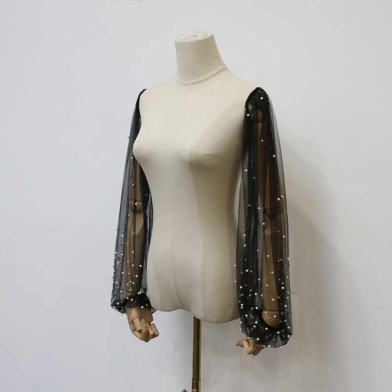 May include: Black sheer sleeves with pearl embellishments. The sleeves are made of a delicate mesh fabric and are adorned with small, white pearls.