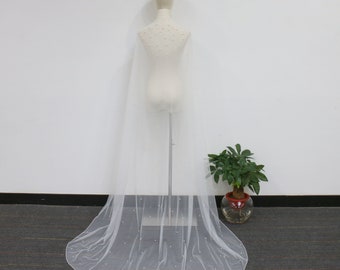 May include: A sheer white bridal veil with scattered pearl embellishments. The veil is draped over a mannequin, showcasing its length and delicate design. The veil's fabric is lightweight and flows gracefully.