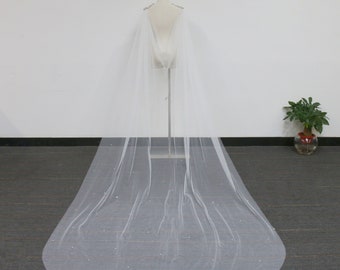 May include: A white tulle bridal cape with a beaded trim. The cape is draped over a mannequin and is shown from the back.