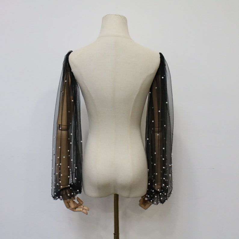 May include: Black sheer mesh sleeves with pearl embellishments. The sleeves are long and have a gathered cuff.