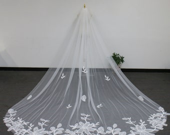 May include: A white bridal veil with a floral design. The veil is made of tulle and features delicate white embroidery of leaves and flowers.