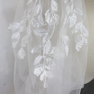 May include: White tulle fabric with white embroidered floral designs. The fabric has a delicate and airy feel.