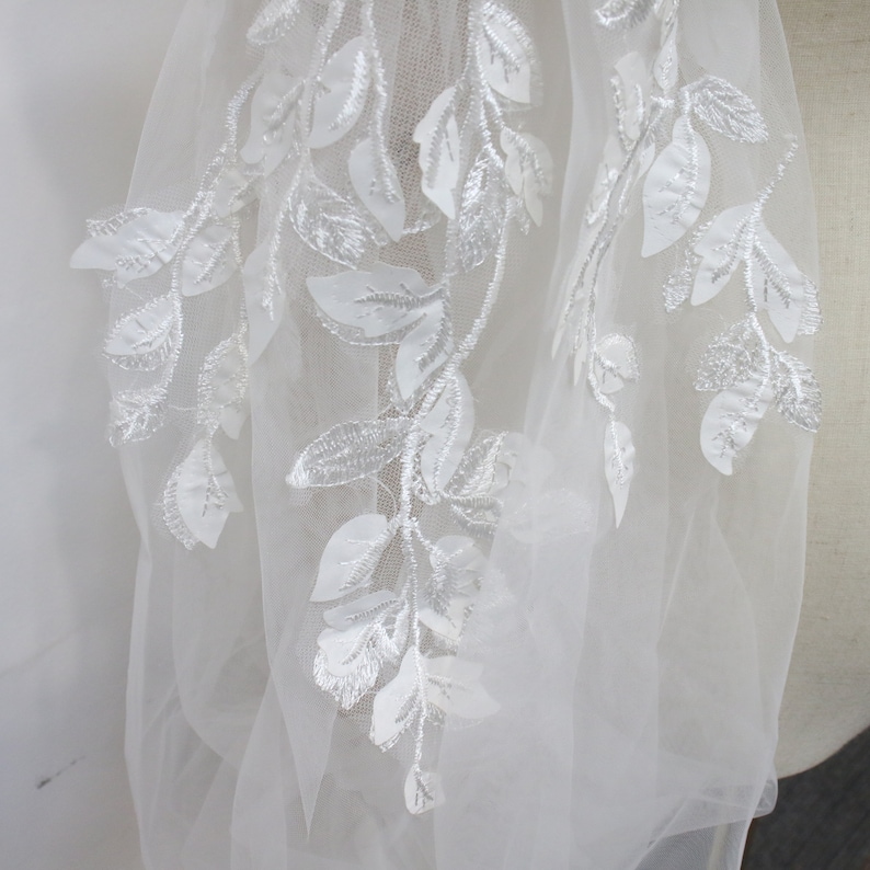 May include: White tulle fabric with white embroidered floral designs. The fabric has a delicate and airy feel.