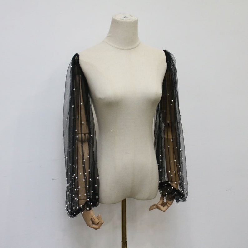 May include: Black sheer mesh sleeves with pearl embellishments. The sleeves are long and have a gathered cuff.