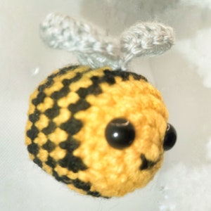 May include: A handmade crochet bee with a yellow and black checkered body, black bead eyes, and gray wings. The bee is a small, whimsical creation, perfect for a child's toy or a decorative item.