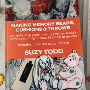 May include: A book cover with an orange background and the title "Making Memory Bears, Cushions & Throws". The book features a step-by-step guide to using loved one's clothing to make keepsakes. The cover includes illustrations of teddy bears and a bunny.