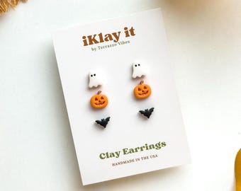 May include: A set of six small clay earrings arranged on a white display card labeled iKlay it by Terrazzo Vibes. The earrings feature miniature white ghosts, orange jack-o'-lantern pumpkins, and black bats. The card reads Clay Earrings.