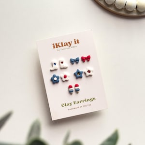 May include: A card featuring handmade clay earrings with patriotic designs. The earrings include stars, bows, and flowers in red, white, and blue. The card reads "iKlay it" and "Clay Earrings, Handmade in the USA."