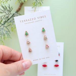 May include: A pair of earrings shaped like Christmas trees, with green, red, and white details, are displayed on a white card. The card reads "TERRAZZO VIBES handmade jewelry" and "MADE IN THE USA".