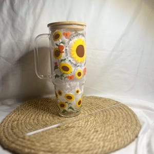 May include: A clear glass tumbler with a bamboo lid and a straw. The tumbler features a sunflower and butterfly design with the text "love, joy, happiness, sunshine".