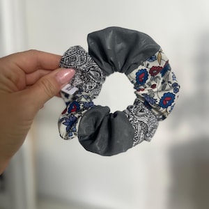 Puede incluir: Una goma para el pelo de tela con una mezcla de estampados y colores. La goma para el pelo presenta una sección de tela gris, una sección con un diseño de cachemira en blanco y negro y una sección con un estampado floral en rojo, azul y blanco.
