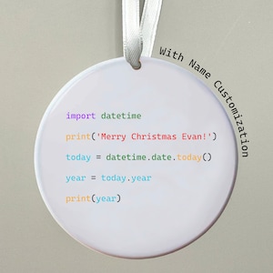 Könnte beinhalten: Ein weißer runder Weihnachtsbaumschmuck mit einem weißen Band. Der Schmuck hat einen Codeausschnitt in verschiedenen Farben darauf gedruckt: lila, grün, gelb, rot und blau. Der Codeausschnitt lautet: "import datetime
print('Merry Christmas Evan!')
today = datetime.date.today()
year = today.year
print(year)"