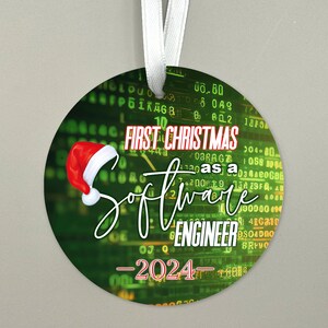 May include: A round green and black Christmas ornament with a red Santa hat and the text "FIRST CHRISTMAS as a SOFTWARE ENGINEER - 2024 - "