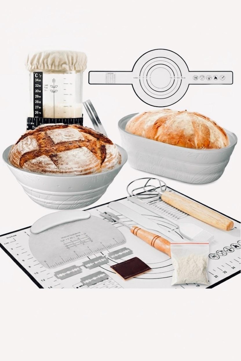 May include: A collection of baking tools and ingredients for making bread. Includes a white bowl with a loaf of bread, a measuring cup, a dough scraper, a baking mat with measurements, and a bag of flour. The bread is golden brown.