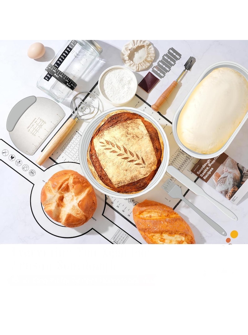 May include: Overhead shot of sourdough bread baking supplies. Includes a loaf of bread with a leaf design, a bowl of flour, a dough scraper, a whisk, a measuring jar, and a loaf of dough in a container.