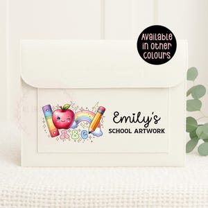 May include: Off-white school artwork folder with a flap. It has a colourful illustration of a winking apple, rainbow, pencil, ruler, and the text "Emily's SCHOOL ARTWORK". A sticker says "Available in other colours".