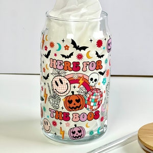 May include: A clear glass tumbler with a Halloween themed design. The tumbler features a colorful pattern of pumpkins, bats, skulls, and the text "Here for the boos".