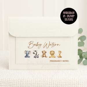 May include: A cream-coloured pregnancy notes organiser with a flap closure. The front has the text "Baby Watson" above watercolour illustrations of an elephant, zebra, monkey, lion, and giraffe. The text "PREGNANCY NOTES" is below.