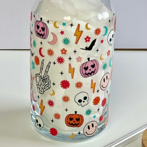 May include: A clear glass tumbler with a Halloween-themed design. The design features a variety of spooky and cute icons, including pumpkins, skulls, bats, stars, and lightning bolts. The tumbler is filled with a white tissue.