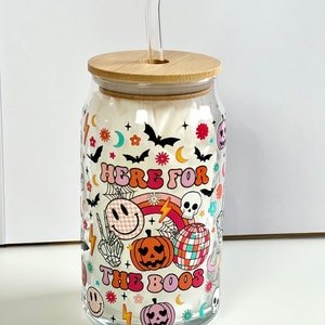 May include: A clear glass jar with a bamboo lid and a straw. The jar has a Halloween-themed design with a rainbow, a skull, a smiley face, and the text "Here for the boos".