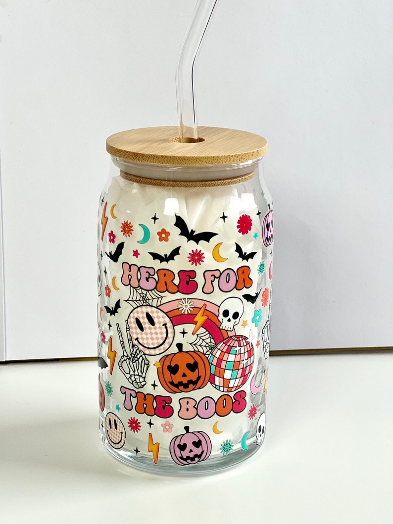 May include: A clear glass jar with a bamboo lid and a straw. The jar has a Halloween-themed design with a rainbow, a skull, a smiley face, and the text "Here for the boos".
