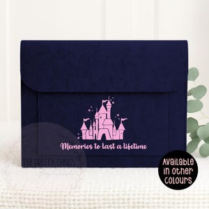 May include: A navy blue felt envelope featuring a pink castle design and the words "Memories to last a lifetime." The envelope has a flap closure and is shown on a white surface. The text "Available in other colours" is also visible.