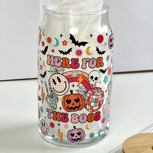 May include: A clear glass can with a Halloween themed design. The can has a white tissue inside and says "Here for the boos" with a rainbow, skulls, pumpkins, and smiley faces.