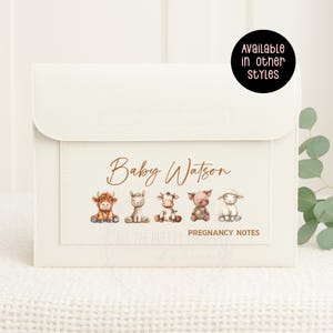 May include: A cream-coloured pregnancy notes organiser with a flap closure. The front features the name "Baby Watson" and illustrations of five farm animals. The text "Pregnancy Notes" is also visible. A circular graphic states "Available in other styles."