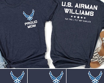 Op de afbeelding: Een set van vier marineblauwe T-shirts met een blauw Air Force-logo en tekst die "Proud Mom", "Proud Dad", "Proud Sister" en "Proud Brother" zegt. De achterkant van een shirt heeft de tekst "U.S. Airman Williams 769 TRS/FLT 007 EAGLES".