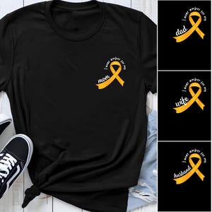 May include: A black t-shirt featuring a yellow awareness ribbon graphic on the left chest. The ribbon is accompanied by the white text "I wear amber for my mom." Additional variations of the graphic include the words "dad," "wife," and "husband."