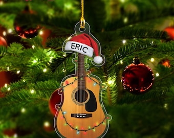 May include: A clear acrylic Christmas ornament shaped like a guitar, decorated with a Santa hat that says "ERIC". The guitar is strung with colorful lights. The text "2D ACRYLIC ORNAMENT" is in a red rectangle at the top.