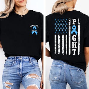 May include: Black t-shirt with a blue ribbon graphic and the words "SUPPORT SQUAD" and "TEAM NAME" on the front. The back features a distressed American flag design with the word "FIGHT" and blue ribbons.