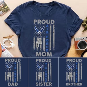 May include: Navy blue t-shirt with a design featuring the words "PROUD AIR FORCE MOM" in white and gray. The design includes an Air Force emblem, a flag, and dog tags. Additional shirts say "DAD", "SISTER", and "BROTHER".