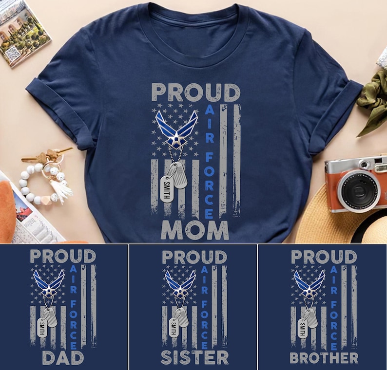 Pu&ograve; includere: T-shirt blu navy con la scritta "PROUD AIR FORCE MOM" in bianco e grigio. Il design include un emblema dell'Aeronautica Militare, una bandiera e targhette identificative. Altre magliette riportano "DAD", "SISTER" e "BROTHER".