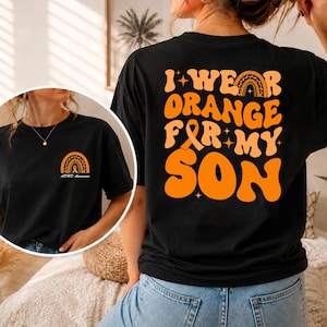 May include: A black t-shirt featuring orange graphic text on the back that reads I WEAR ORANGE FOR MY SON with an orange awareness ribbon and rainbow icon. The front chest area displays a smaller matching orange rainbow and ribbon icon.
