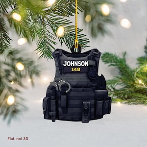 May include: Black and grey Christmas bauble shaped like a police officer's tactical vest with the name "JOHNSON" and the number "148" printed on the front.